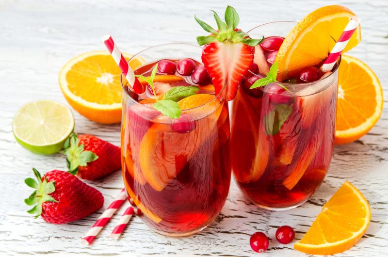 Two glasses with fruit punch, including straws and sliced fresh fruit