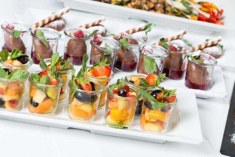 White plates on a table at a party that contain desserts, including fruit salad and chocolate mousse