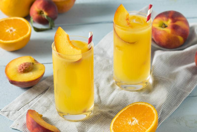 Two glasses of a fuzzy navel cocktail with peaches and oranges