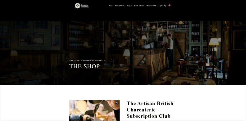 screenshot of GB Charcuterie The Artisan British Charcuterie Subscription Club's, black header on top with the website's logo and main menu followed by darken image banner showing a rustic looking shop, the page is showing details of the subscription plan accompanied by an image.