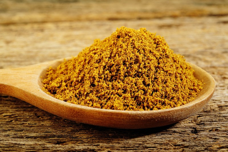 closeup image of a wooden ladle full of garam masala, resting on a wooden surface