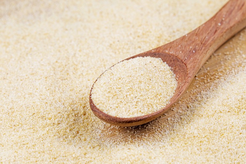 closeup image of a wooden ladle full of garlic powder on a surface full of garlic powder