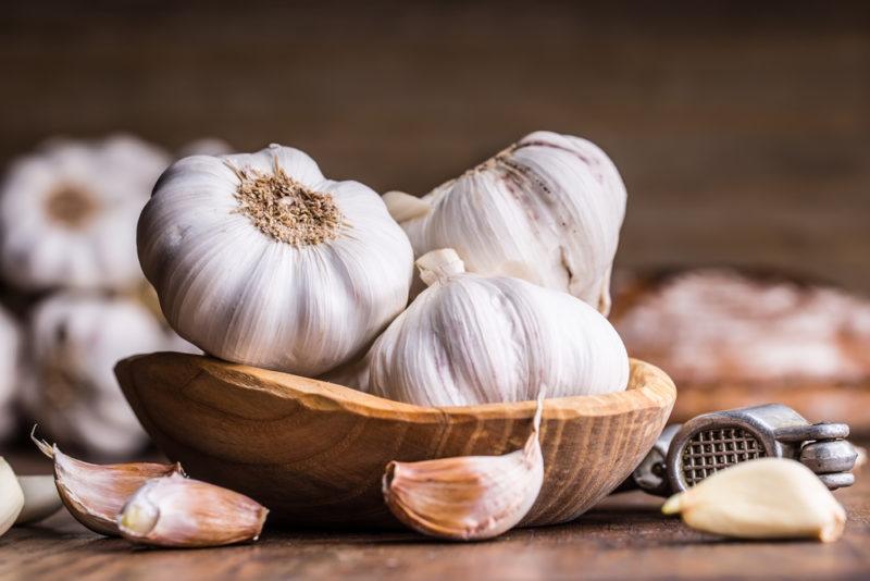 A shallow wooden bowl with fresh heads of garlic and a few garlic cloves scattered around