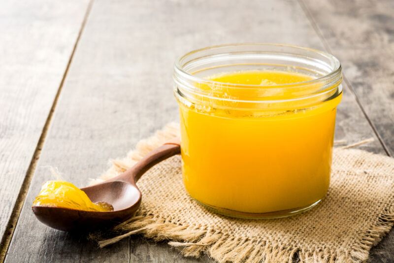Ghee,Or,Clarified,Butter,In,Jar,And,Wooden,Spoon,On | Food For Net This photo shows a jar of yellow ghee next to a spoon of ghee on a piece of burlap cloth, resting on a wooden table.