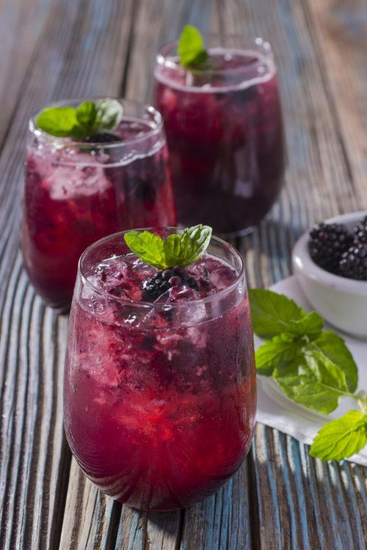 Three glasses of a gin and tonic with muddled blackcurrants