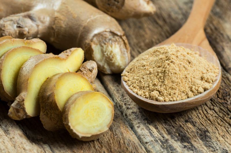 A spoon of ginger with sliced ginger and ginger powder