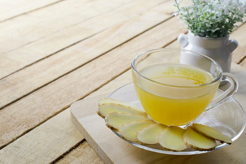 A small glass with ginger juice next to sliced ginger