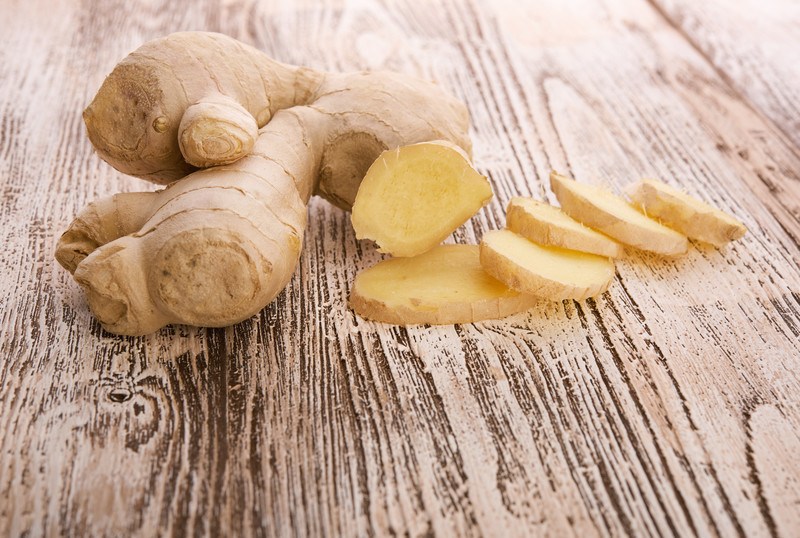 A whole ginger root and six slices of ginger rest on a rustic wooden board.