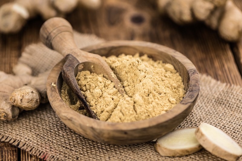 wooden bowl and scoop full of ginger powder with burlap cloth, with fresh ginger and sliced ginger around it