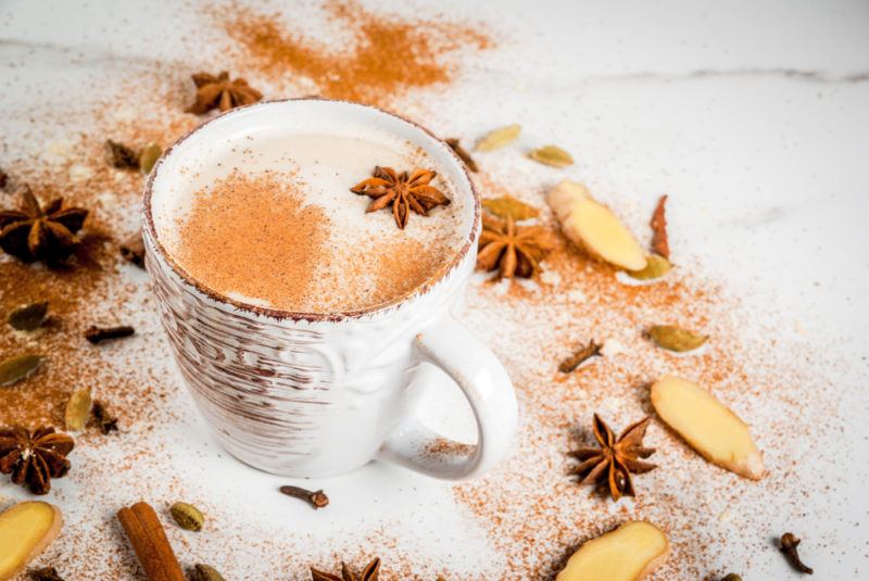 A mug of ginger tea latte on a table with spices scattered around