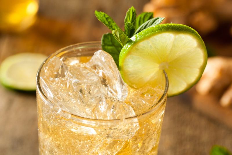 A glass of ginger beer with ice, a slice of lime and a garnish