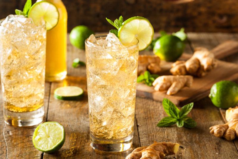 A glass of ginger beer with ice and limes