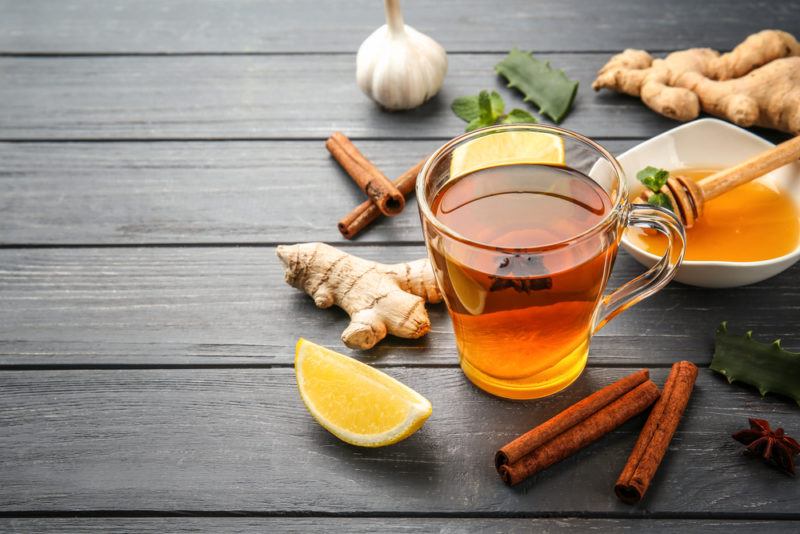 A glass of ginger cinnamon tea on a table with the ingreidents scattered around