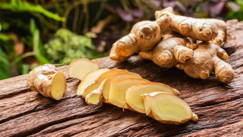 A wooden table with a whole ginger root and some sliced ginger