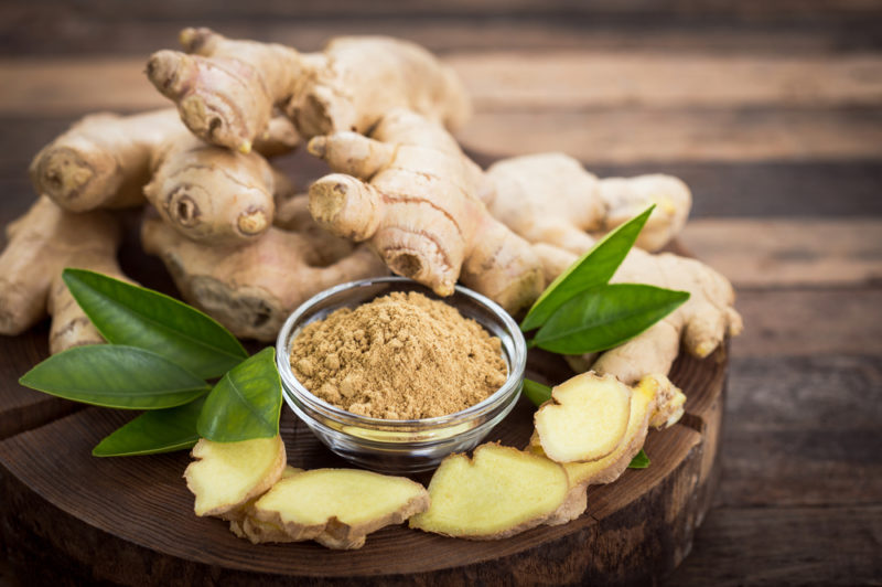 A wooden board with ginger root, ginger powder and sliced ginger