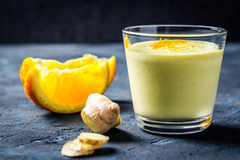 A glass with a ginger smoothie next to ginger and citrus