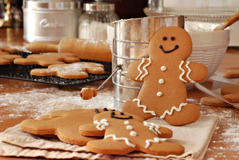 A gingerbread man standing up against a bowl, with more gingerbread men lying down flat