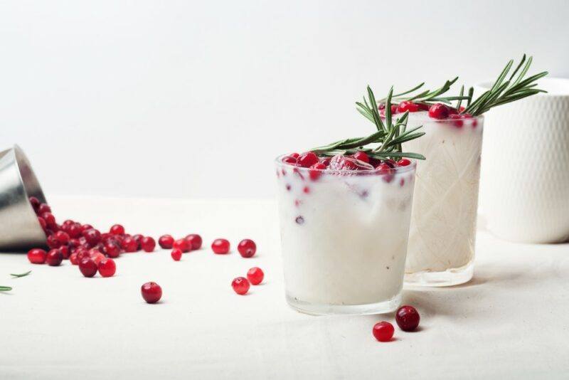 Two glasses of a coconut white Christmas margarita, with cranberries and pine needles as a garnish