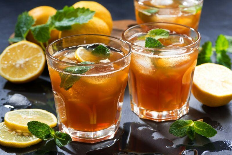 Three glasses of a midnight fever cocktail with ice, with lemons and greenery on a table