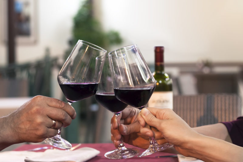 People sitting at a table toasting with glasses of red wine