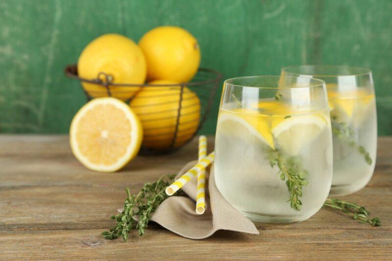 Two glasses of lemon water with ice, with a basket of lemons in the background