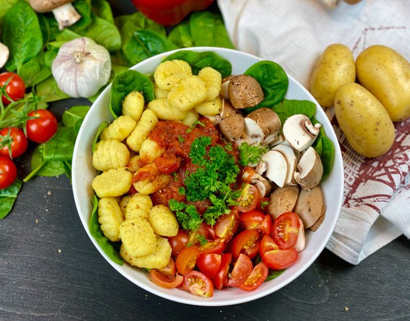 A white bowl that contains gnocci and various veggies