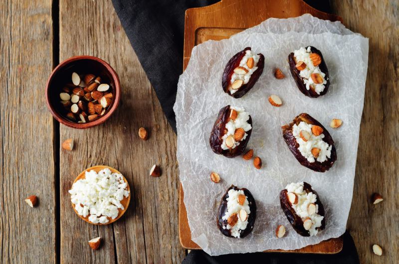 A wooden board with parchment paper that has some goat cheese appetizers, next to a small bowl of goat cheese and another of nuts