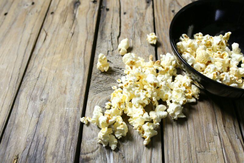 A black bowl containing black pepper and goat milk popcorn, where some has spilled out onto the table