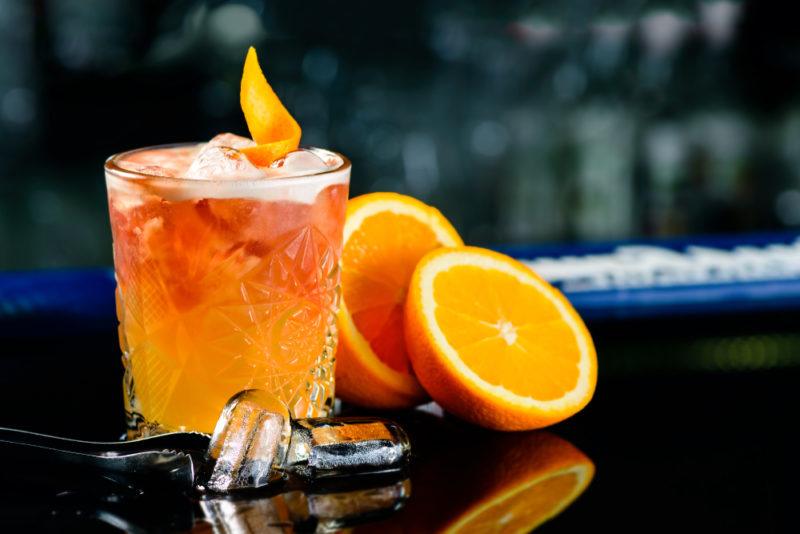 A glass containing a Godfather cocktail, with sliced oranges next to it