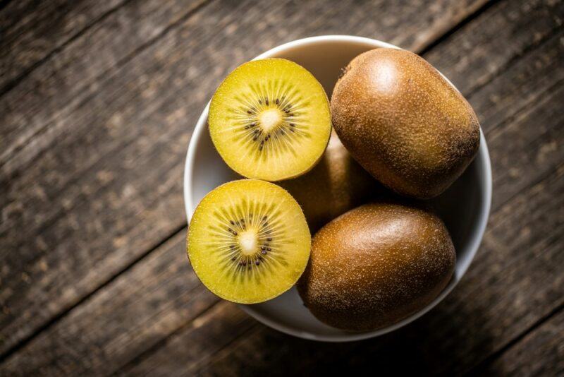 A small bowl containing a few whole golden kiwis and two golden kiwi halves