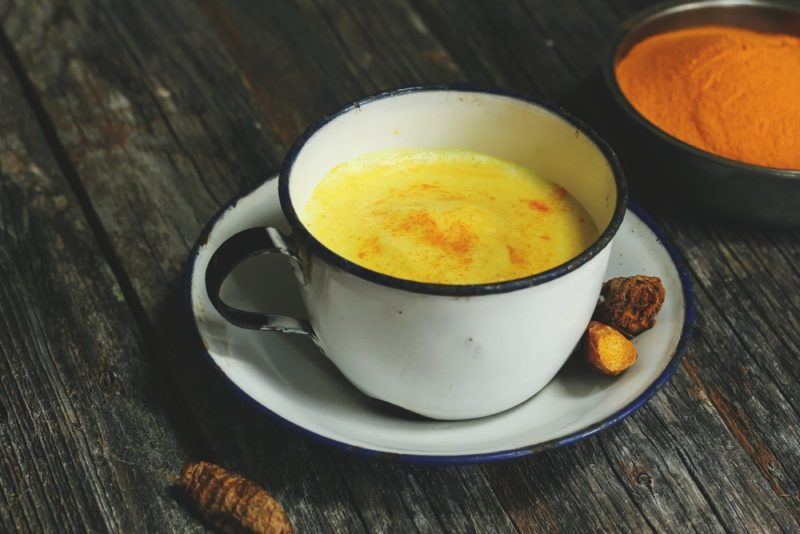 A white mug of golden milk with a black bowl of turmeric