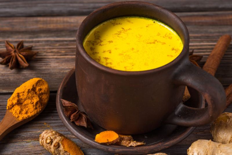 A dark colored mug contianing golden milk, with turmeric, star anise and other spices on the table