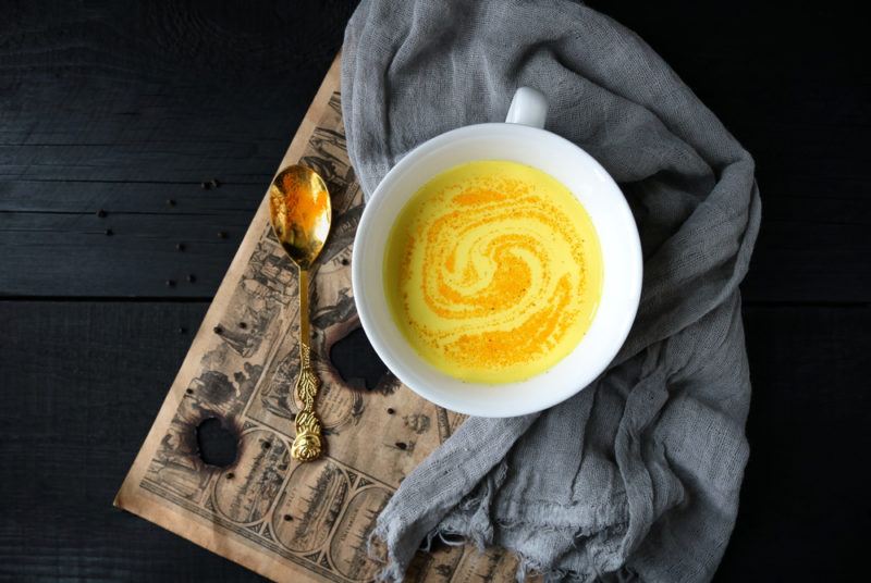 A mug of golden milk on a wooden board with a spoon and a cloth