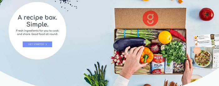 A blue background with a cardboard box containing various vegetables