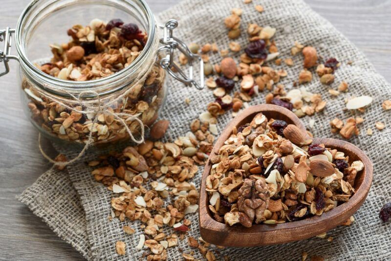 A jar of granola, granola in a heart-shaped bowl and more scattered on a table