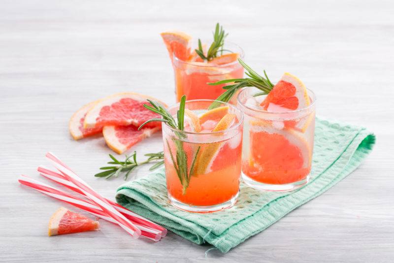 Three glasses with grapefruit juice and ice, with sliced grapefruit and straws on the table