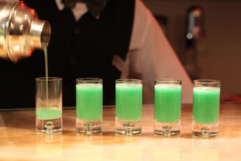 Various green shots being poured by a barkeeper