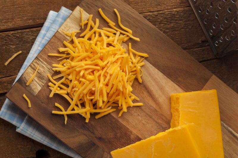 A wooden board with grated colby cheese and blocks of colby cheese