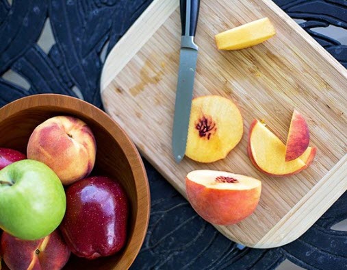 Apples in a bowl and a peach on a cutting board