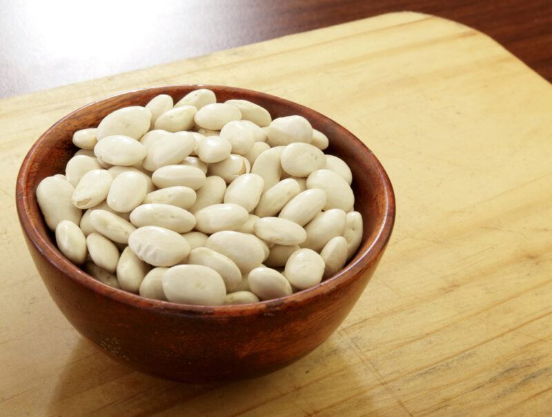 on a wooden board is a dark brown wooden bowl full of Great Northern beans