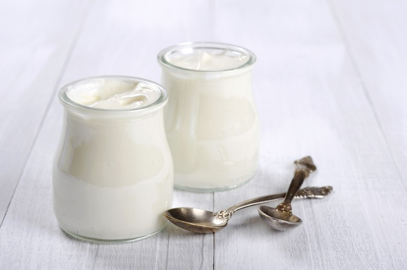 on a white wooden surface is a couple of jar full of yogurt with two silver spoons