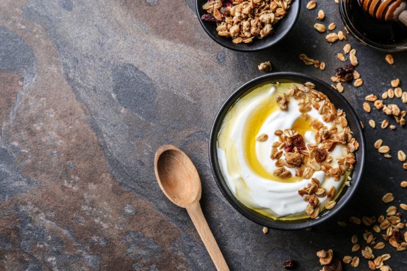 A bowl of Greek yogurt that contains honey and nuts, along with a wooden spoon