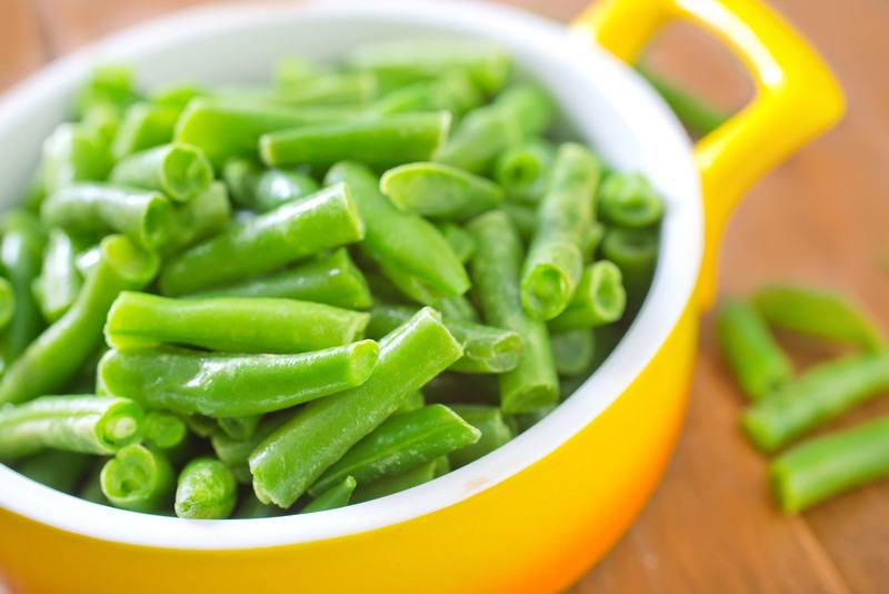 A yellow ceramic dish is filled with green beans.