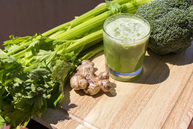 A glasss of green juice next to ginger and some greens