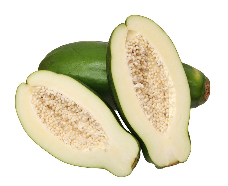 A halved green papaya rests against a whole green papaya in front of a white background.