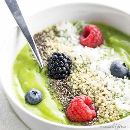 A bright green smoothie in a bowl with various toppings