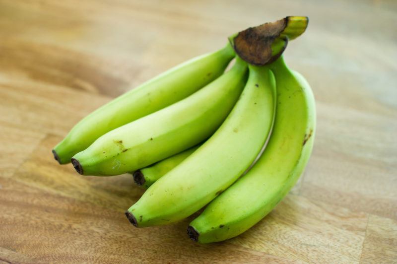 A bunch of green bananas on a light wooden table