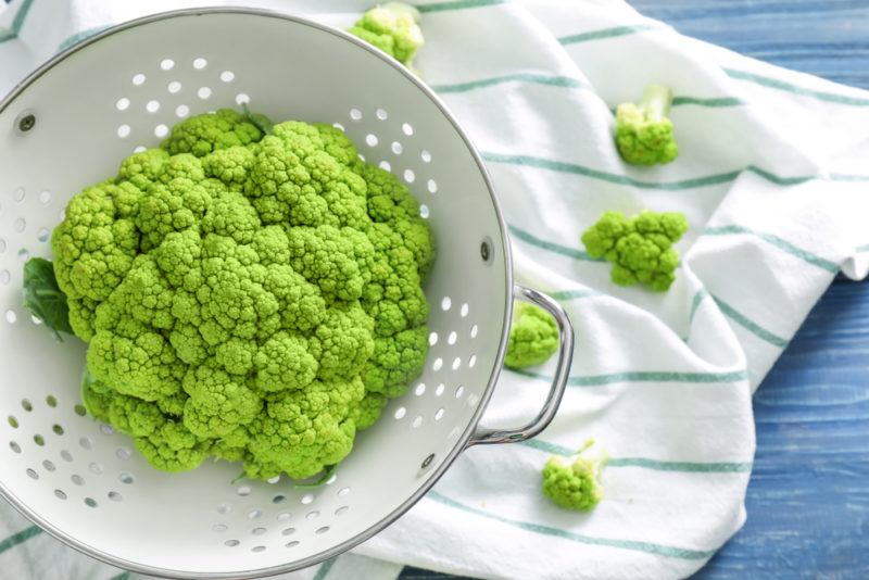 Green cauliflower in a colander with a tea towel underneath