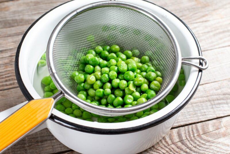 A blue and white dish with a sieve that's being used to drain green peas