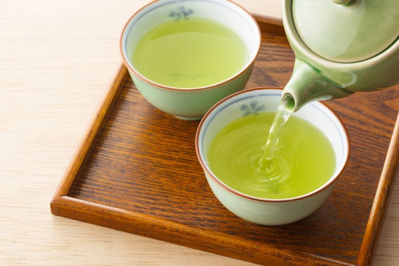 Green tea being poured into two mugs on a wooden board